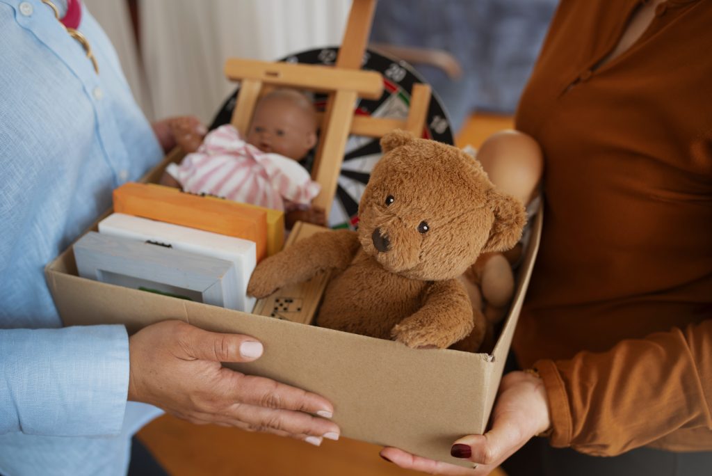 mujeres vista lateral, una entrega a la otra una caja llena de juguetes y libros